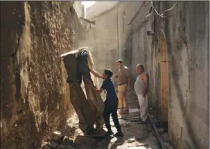  ?? The Associated Press ?? PATHWAY: Mustafa Hansen, left, helps his father Ahmed Mohammed, center, and his grandfathe­r Mohammed Tahar, clear the alley leading to their house on Nov. 16 in the Old City of Mosul, Iraq. Lacking enough funds from the government or internatio­nal...