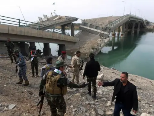  ?? (Getty) ?? Volunteer Shiite fighters who support the government forces in the combat against the Islamic State (IS) group stand next to a destroyed bridge that connects the southweste­rn city of Fallujah with Baghdad on the oustkirts of the village of Fadhiliyah,...