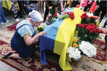  ?? The Associated Press ?? ■ A woman kneels at activist and soldier Roman Ratushnyi’s coffin during his memorial service in Kyiv, Ukraine, on Saturday. Ratushnyi died in a battle near Izyum, where Russian and Ukrainian troops are fighting for control of the area.