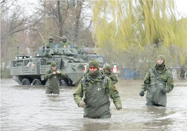  ?? RYAN REMIORZ / THE CANADIAN PRESS ?? Canadian Forces personnel wade through flooded streets in Deux-Montagnes, Que. More than 1,500 soldiers arrived Monday to help Quebecers.