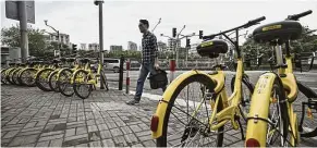  ??  ?? Global expansion: A pedestrian walks past parked Ofo bicycles on a sidewalk in Shanghai. The company is eyeing global expansion amid rising domestic expansion.