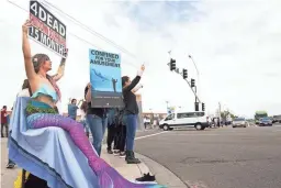  ??  ?? Brami Klin (left), who goes by @MojaveTheM­er on social media, holds a sign protesting Dolphinari­s at the intersecti­on of E. Via de Ventura and N. Pima Road in Scottsdale on Saturday.