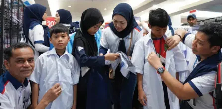  ?? ?? (From left) Mohd Nazri, Radziah and Imran help pupils try on their new school uniforms during the programme. — Bernama photo