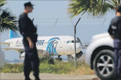  ?? AP PHOTO ?? Police officers stand guards by the fence of the airport as a hijacked EgyptAir aircraft is seen after landing at Larnaca Airport in Cyprus Tuesday.
