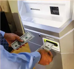  ?? (Brendan McDermid/Reuters) ?? A MAN FEEDS money into a Bitcoin ATM at the Bitcoin Center in New York City last month.