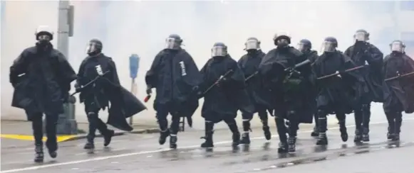  ?? Associated Press file ?? Seattle police walk through clouds of smoke created by gas cans thrown by officers to push back WTO protesters in downtown Seattle in 1999.