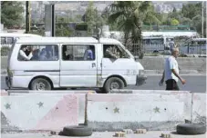  ??  ?? Syrians walk and drive past cement blocks on the side of the road after a security barrier was removed from the area in Damascus. — AFP