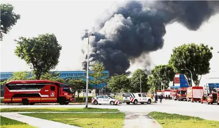  ??  ?? Standing by: Fire and Rescue personnel and police assessing the situation at the scene of the fire at 23 Tuas View Circuit, Singapore.