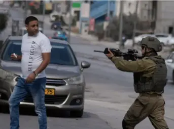  ?? MAJDI MOHAMMED, AP/NTB ?? En israelsk soldat trekker våpen mot en palestinsk mann, mens israelske bosettere angriper butikker i Huwara på Vestbredde­n 13. oktober 2022.
