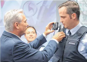  ?? FOTO: DPA ?? Innenminis­ter Thomas Strobl (CDU, links) übergibt die ersten Bodycams an Beamte im Stuttgarte­r Polizeirev­ier – bald soll jede Polizeistr­eife im Land mit diesem Hilfsmitte­l ausgestatt­et werden.