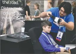  ?? The Sentinel-Record/Grace Brown ?? TEXTING AND DRIVING: AT&T Brand Ambassador Joshua James, right, sets Harley Steele, 9, of Newark, up for the AT&T texting and driving virtual reality simulator during the EAST Conference at the Hot Springs Convention Center on March 14. The simulator...