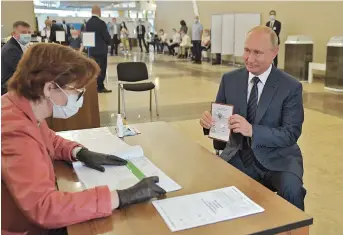  ??  ?? Russian President Vladimir Putin shows his passport to a member of a local electoral commission as he arrives to cast his ballot in a nationwide vote on constituti­onal reforms at a polling station in Moscow on Wednesday. — AFP