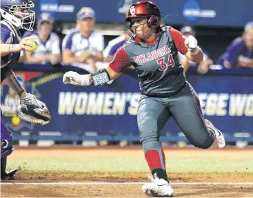  ?? [PHOTO BY SARAH PHIPPS, THE OKLAHOMAN] ?? Oklahoma’s Fale Aviu, right, avoids the tag of Washington catcher Morganne Flores and scores on a squeeze bunt during the second inning of a Women’s College World Series softball game at Hall of Fame Stadium. OU beat the Huskies, 3-1.