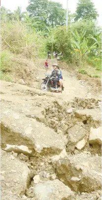  ?? SUNSTAR FOTO / ALLAN DEFENSOR ?? DANGER. On board a motorcycle-forhire, a resident of Sitio Langob in Barangay Sirao, Cebu City passes by a road that was damaged by a landslide.