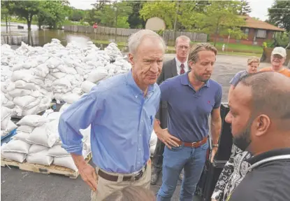  ?? | PAUL VALADE/ DAILY HERALD VIA AP ?? Gov. Bruce Rauner pauses near hundreds of sandbags and the flooded McClure Avenue with Lake County Board Chairman Aaron Lawlor and IEMA Director James Joseph ( right) on Friday in Gurnee.