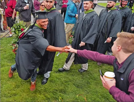  ?? SEAN D. ELLIOT/THE DAY ?? Graduate Khaliyl Holland, left, shakes hands with former soccer teammate Andrew Nigro as the Class of 2018 marches in for the 74th commenceme­nt exercises at Mitchell College on Saturday in New London. Visit www.theday.com for a gallery from the ceremony.