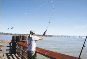  ??  ?? David Ducay wears a hooded cap to stay cool in the sun while fishing for striped bass on the pier in Martinez. The East Bay is expected to cool down about 10 degrees Thursday and drop even more on the weekend.