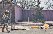  ?? ?? A Ukrainian soldier passes the covered bodies of Tatyana Perebeynos and her two children, killed by Russian mortar rounds as they tried to flee Irpin last Sunday