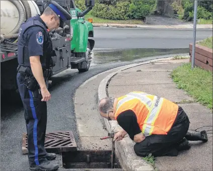  ?? SAM MCNEISH/THE TELEGRAM ?? An RNC officer and a member of Rovers Search and Rescue examine a storm sewer at the corner of Alderberry Lane and Mundy Pond Road in search of clues stemming from a stabbing on Thursday.