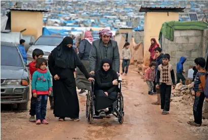  ?? — AFP ?? A disabled syrian woman from the province of Hama is pushed on a wheelchair through a muddy road following torrential rain that affected a camp for displaced people near the town of Atme close to the Turkish border in Idlib province on Thursday.