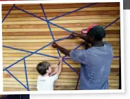  ??  ?? ABOVE Angus helps Paul Chipeta to apply blue masking tape in a geometric pattern on the sanded garage door.