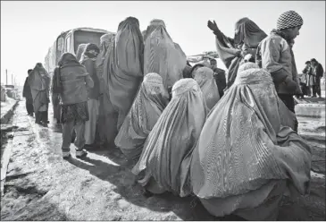  ?? ASSOCIATED PRESS ?? Afghan women wait to receive winter relief assistance donated by the United Nation’s refugee agency outside a refugee camp in Kabul on Sunday. About 600 displaced families in the camp received relief from the agency.