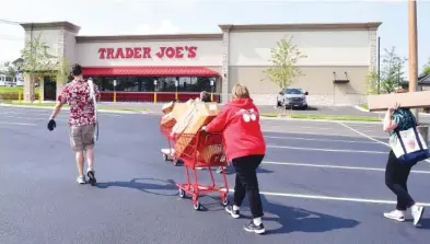  ?? STAFF PHOTO BY ROBIN RUDD ?? Trader Joe’s employees carry supplies into the store across a recently sealed parking lot on Monday. The new Trader Joe’s on Gunbarrel Road has signage up as the store nears its grand opening.