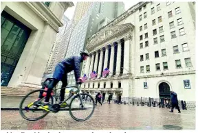  ?? AP ?? A bicyclist rides by the New York Stock Exchange.