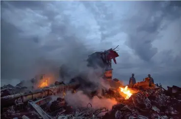  ?? Associated Press file ?? People walk among the debris at the crash site of the Malaysia Airlines Flight 17 passenger plane near the village of Grabove, Ukraine, in July 2014.