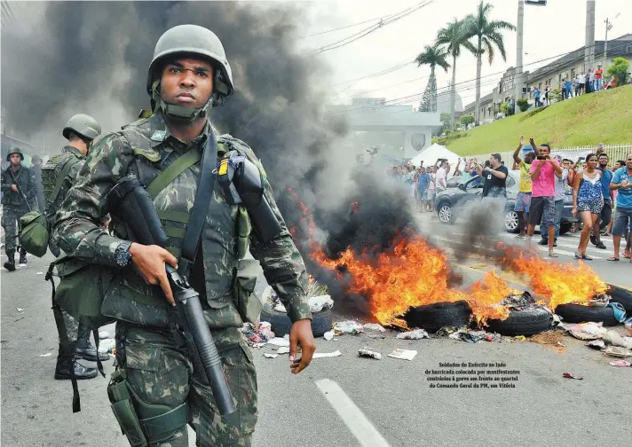  ??  ?? Soldados do Exército ao lado de barricada colocada por manifestan­tes contrários à greve em frente ao quartel do Comando Geral da PM, em Vitória