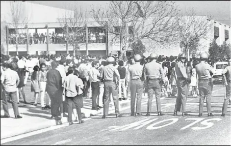  ??  ?? SHERIFF’S DEPUTIES form a line near Garfield High School on March 5, 1968, the day of the first of the Eastside student “blowouts.” By the time the walkouts peaked a week later, 22,000 students had joined in. “Education, not eradicatio­n!” was a...