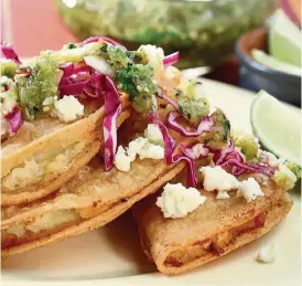  ??  ?? Fried potato- filled tacos topped with fresh cabbage, queso fresco and tomatillo salsa.