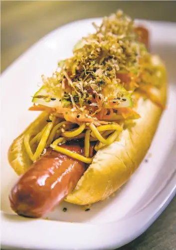  ?? Photos by John Storey / Special to The Chronicle ?? Takuya Japanese Hotdog and Bowl in the Inner Sunset offers the Kimdle, above, topped with yakisoba noodles, and the Gyufire, left, which tops a Cajun sausage with beef and pineapple.