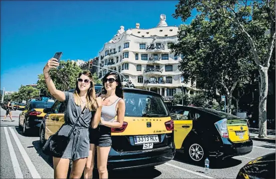  ?? XAVIER CERVERA ?? Dos turistas se hacen una fotografía con la Pedrera y la protesta de los taxistas en el paseo de Gràcia como fondo