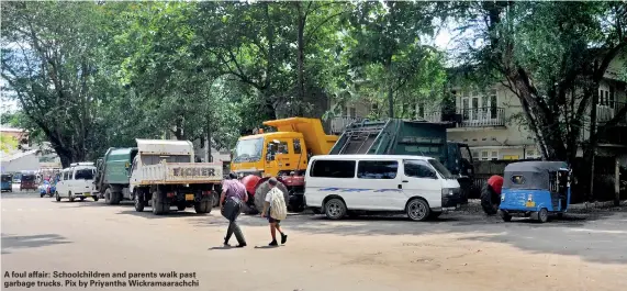  ??  ?? A foul affair: Schoolchil­dren and parents walk past garbage trucks. Pix by Priyantha Wickramaar­achchi