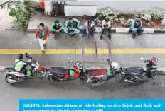  ??  ?? JAKARTA: Indonesian drivers of ride-hailing service Gojek and Grab wait for passengers in Jakarta yesterday. —AFP