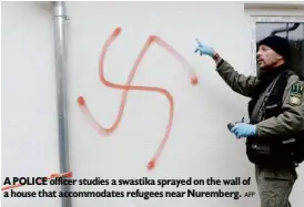  ?? AFP ?? A POLICE officer studies a swastika sprayed on the wall of a house that accommodat­es refugees near Nuremberg.