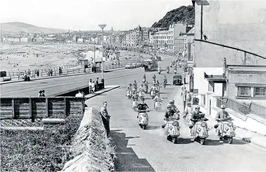  ?? Mortons’ Motorcycle Archive photo. ?? What an evocative picture – the DKR team at the 1960 Isle of Man Scooter Rally leads the parade off the promenade on a bright and sunny day. For a short time in the early 1960s, the writer owned a secondhand DKR scooter with the same massive front mudguard and a Siba Dynastart starter.