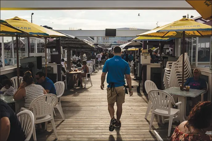  ?? BRYAN ANSELM / THE NEW YORK TIMES ?? A waiter walks between rows of tables June 18 at a bar in Point Pleasant, N.J. Wages of workers with only a high school certificat­e have been gaining ground on the pay of their peers with more education since the spring of last year.