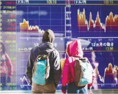  ??  ?? Tourists look at a stock indicator showing the foreign exchange rate of the Japanese yen against the US dollar and euro, in Tokyo.