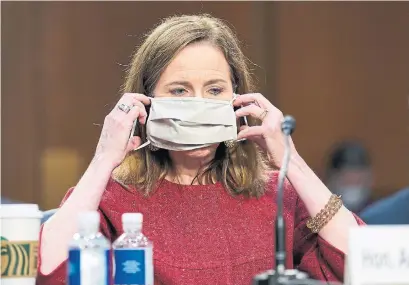  ?? SUSAN WALSH THE ASSOCIATED PRESS POOL ?? Supreme Court nominee Amy Coney Barrett puts on a face mask during a break in her Senate confirmati­on hearing.
