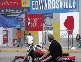  ?? LAURIE SKRIVAN St. Louis Post-Dispatch/TNS) ?? A motorist watches owner Daniel Ricketts, left, and muralist Jerome Lamke with St. Louis Sign & Mural, paint a Route 66 mural on a building at the southeast corner of East Vandalia and South Main streets on July 25 in Edwardsvil­le, Ill. The mural is among a series of murals highlighti­ng Route 66 in Southern Illinois towns.