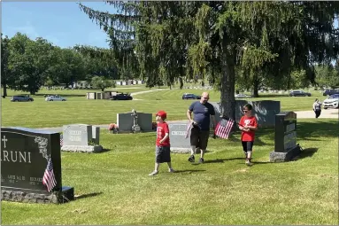  ?? RACHEL RAVINA — MEDIANEWS GROUP ?? Michael Sasso, center, of Lansdale, walks through Calvary Cemetery with his sons, Julien, 8, and Michael, 10, helping to plant flags at the West Conshohock­en cemetery ahead of Memorial Day.