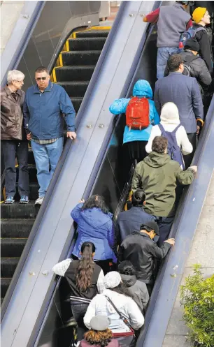  ?? Michael Macor / The Chronicle ?? Riders take the escalator as they exit the Powell Street BART Station, some standing to the right while others walk past on the left.