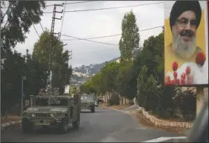  ?? The Associated Press ?? LEBANON: Lebanese army vehicles pass next to a portrait of Hezbollah leader Sayyed Hassan Nasrallah, as they patrol on a road that leads to the site of an explosion that rocked a Hezbollah stronghold, in the southern village of Ain Qana, Lebanon, Tuesday. The powerful explosion sent thick grey smoke billowing over the village, but the cause was not clear.