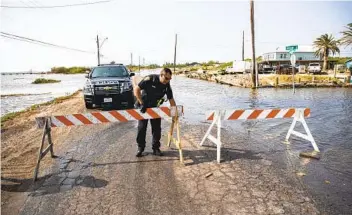  ?? COURTNEY SACCO AP ?? A Corpus Christi police officer places a barricade to close Laguna Shores Boulevard due to flooding on Sunday in Corpus Christi, Texas, as Tropical Storm Beta heads toward Texas and Louisiana.