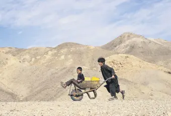  ?? ?? A boy pushes a wheelbarro­w filled with canisters and his younger brother to collect water from a stagnant pool, about 3 kilometers from their home in Kamar Kalagh village, Herat, Afghanista­n, Nov. 26, 2021.