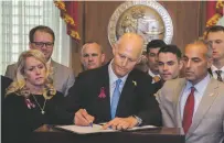  ?? MARK WALLHEISER/THE ASSOCIATED PRESS ?? Florida Gov. Rick Scott signs the Marjory Stoneman Douglas Public Safety Act in the governor’s office Friday in Tallahasse­e. Scott is flanked by victims’ parents Gena Hoyer, left, and Andrew Pollack, right.