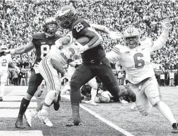  ?? Mike Mulholland / Getty Images ?? Running back Hassan Haskins scores one of his five touchdowns for Michigan, which clinched a spot in the Big Ten championsh­ip game and kept its College Football Playoff hopes alive.