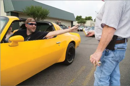  ?? Staff photos by Joshua Boucher ?? A man in a Trans-Am reaches for a Coors beer that Rickey Richardson moves just out of his reach Sunday on Broad Street in Texarkana, Ark. Board members of the Four States Auto Museum gave drivers in the Bandit Run 2017 a symbolic Coors before they...